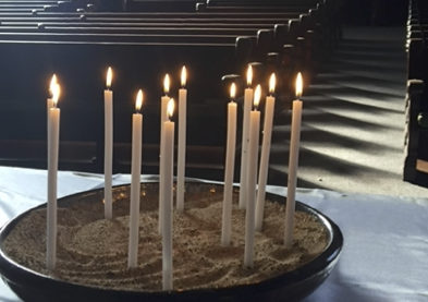 A shallow bowl of sand with many lit candles burning.