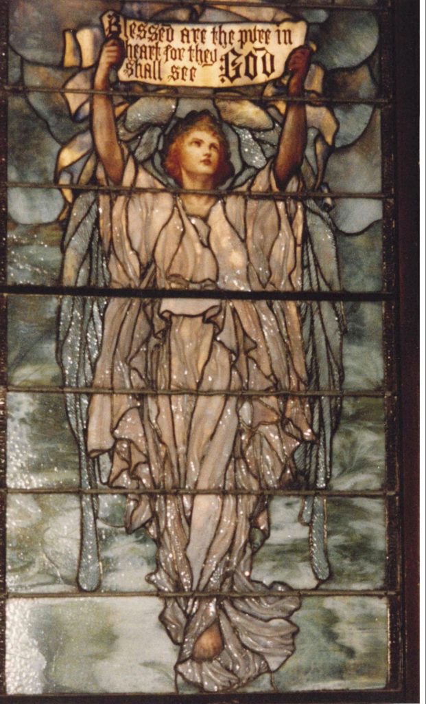 Stained glass image of an angel in white robes holding a banner that reads Blessed are the pure in heart for they shall see God.